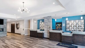 A modern reception area with a wooden floor, a central column, and a reception desk with a blue accent wall. - Wyndham Garden Kenosha Harborside (Kenosha)