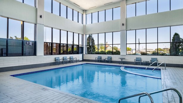 An indoor swimming pool with clear views through large windows, tiled flooring, and a few lounge chairs. - Wyndham Garden Kenosha Harborside (Kenosha)