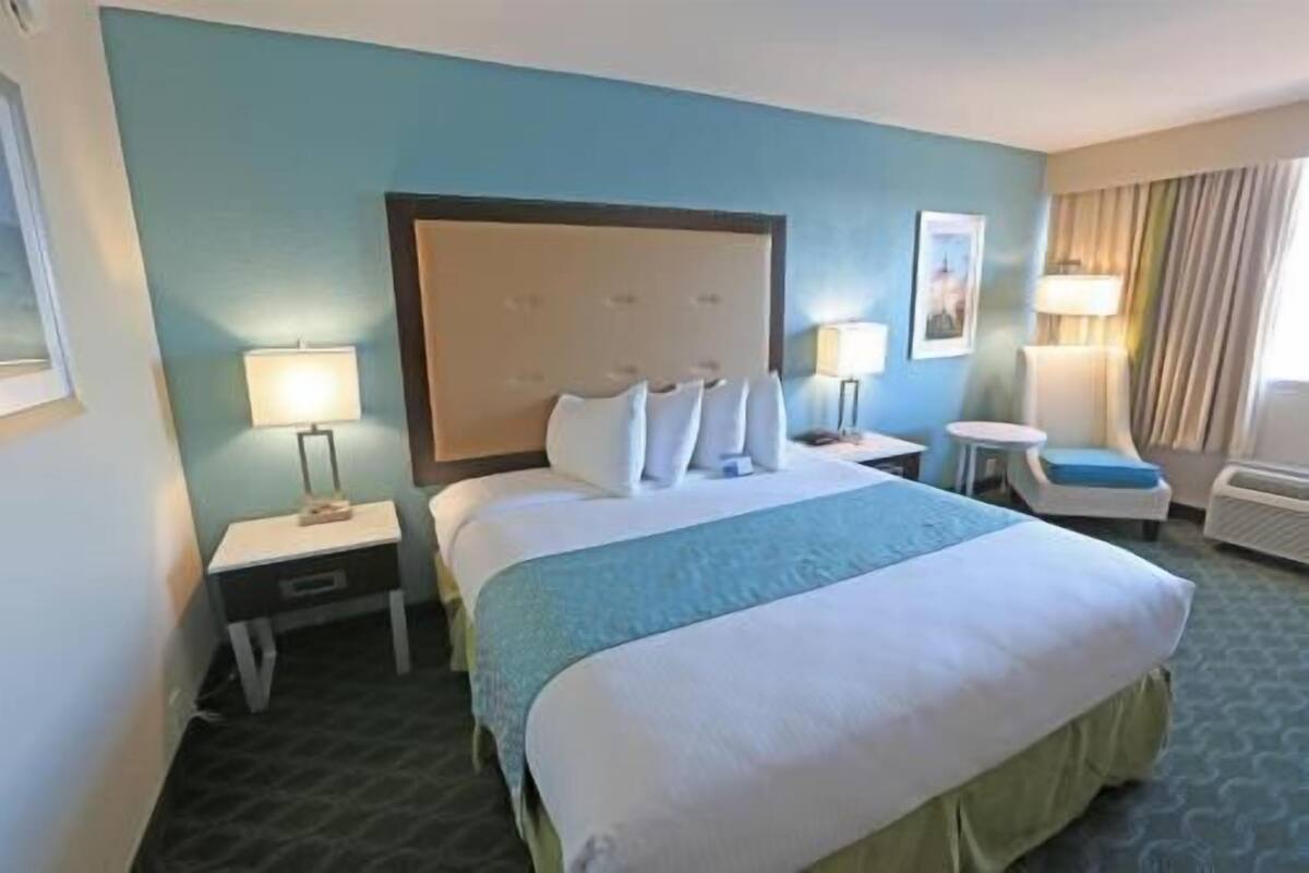 Ein Hotelzimmer mit einem großen Bett, zwei Nachttischen, einem Sessel und einer Lampe.
