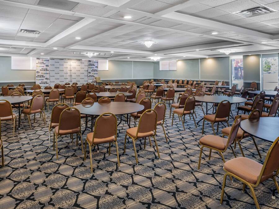 A conference room with multiple tables and chairs, a patterned carpet, and a ceiling with recessed lighting.