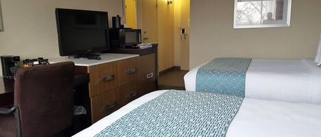 A hotel room with a desk, a television, a bed with patterned bedding, and a framed picture on the wall.