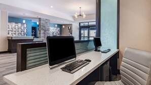 A modern reception desk with a computer, keyboard, and mouse. There are cushioned seating areas and a decorative wall in the background. - Wyndham Garden Kenosha Harborside (Kenosha)