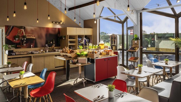 Un restaurante moderno con techo alto, vigas a la vista y amplios ventanales.