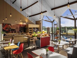 A modern restaurant with a high ceiling, exposed beams, and large windows. - ibis Saint Nazaire Trignac (Trignac)