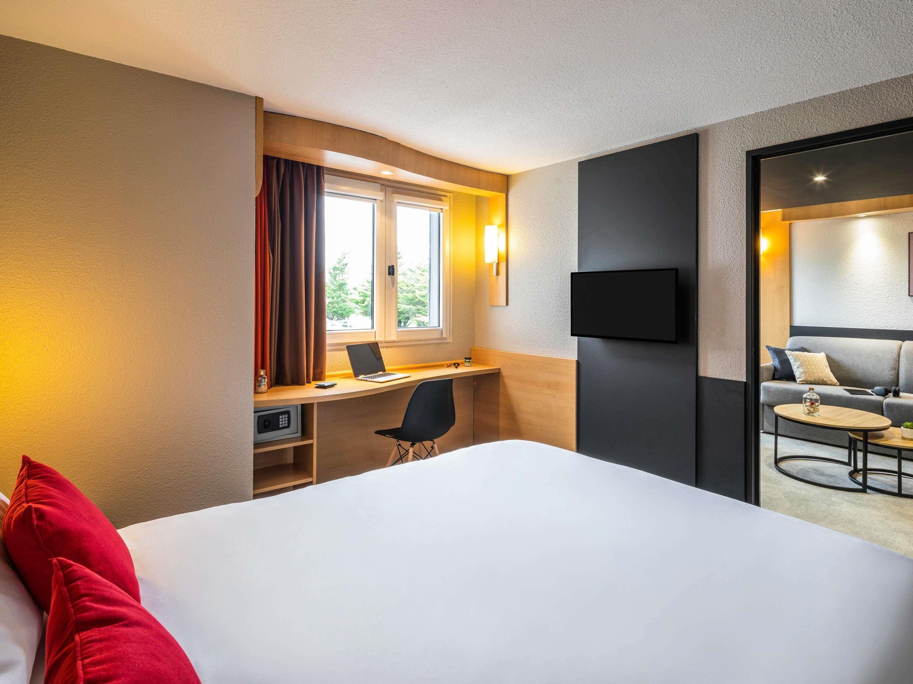 Una habitación de hotel con cama, escritorio con computadora portátil, silla, televisor y una pequeña mesa con una planta.