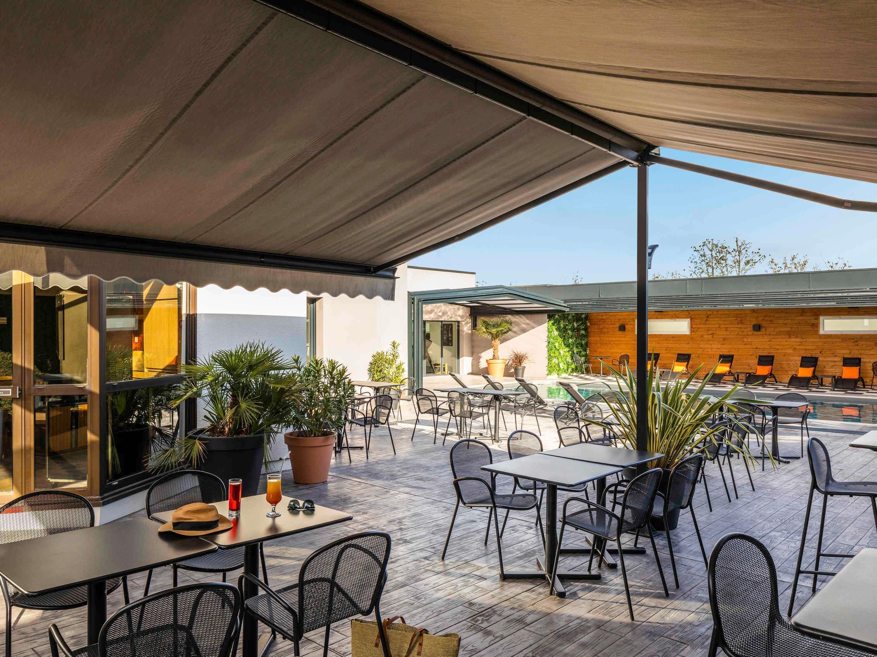 Une terrasse extérieure avec des tables et des chaises, des plantes en pot et un espace piscine.