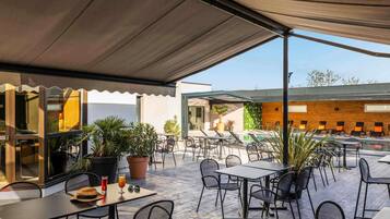 Une terrasse extérieure avec des tables et des chaises, des plantes en pot et un espace piscine.