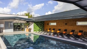 Una piscina interior con suelo a cuadros, tumbonas y una pared de madera con ventanas.