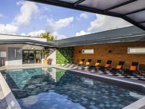 An indoor swimming pool with a checkered floor, sun loungers, and a wooden wall with windows. - ibis Saint Nazaire Trignac (Trignac)