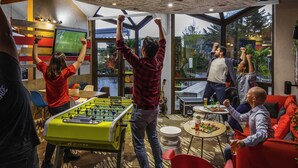 Un espacio interior dinámico con una mesa de fútbol de mesa, un ventanal que ofrece vistas al exterior y un techo con diseño circular que incluye texto e ilustraciones.