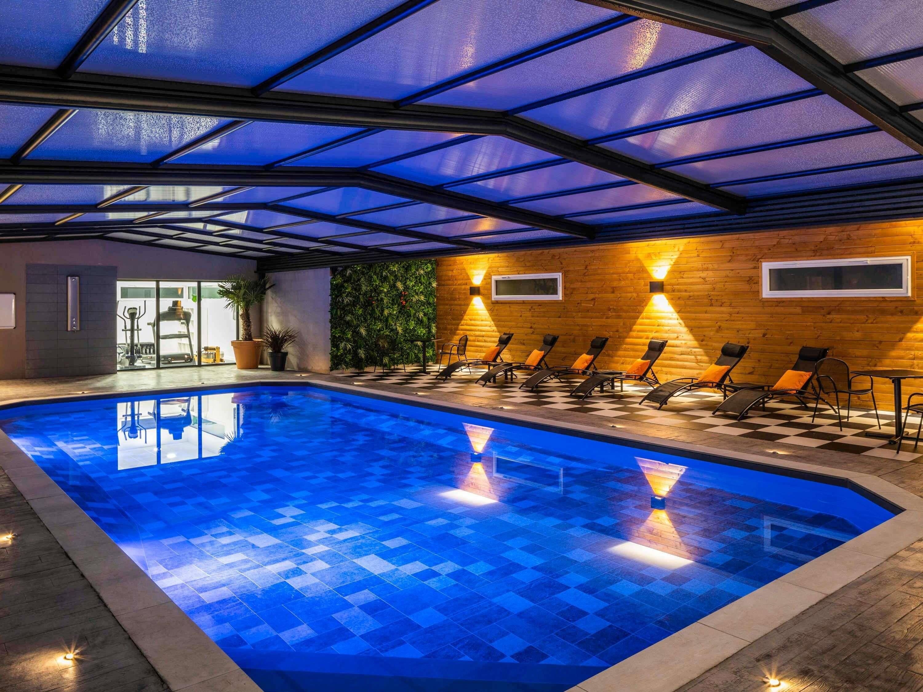 An indoor swimming pool with a checkered floor, lounge chairs, and a wooden wall with a green wall feature.