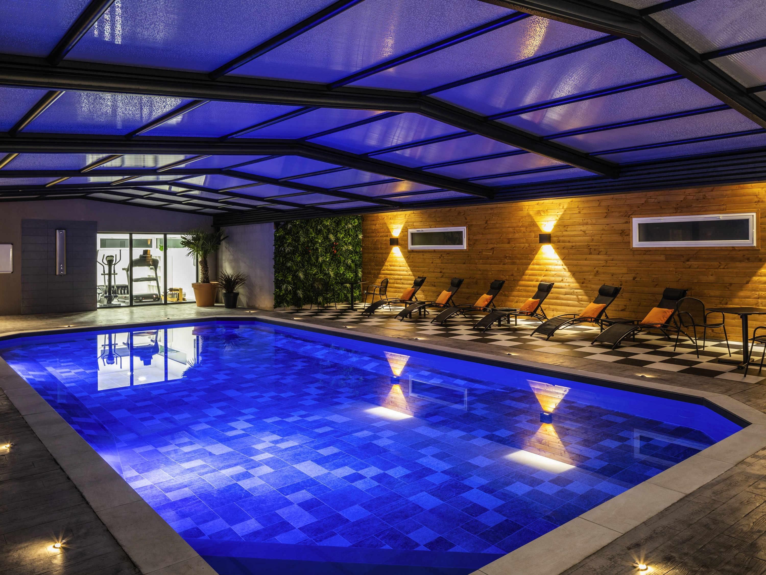 Une piscine intérieure avec un sol à carreaux, des chaises longues et un mur en bois doté d’une fenêtre.