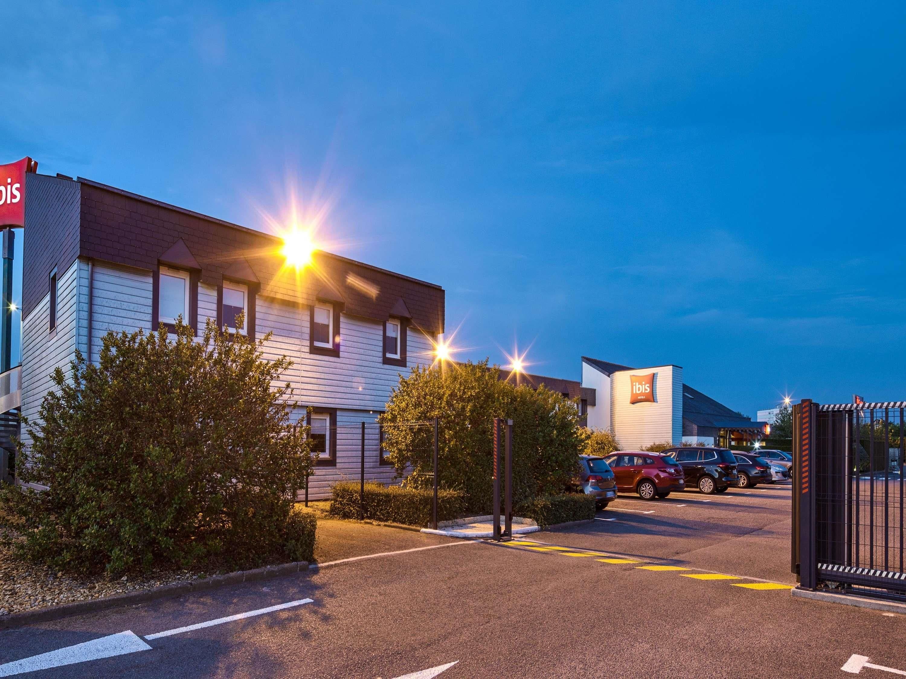 A hotel with a modern design, featuring a parking lot and a gated entrance.
