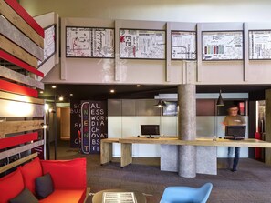 A modern office space with a central desk, seating area, and a large pillar. - ibis Saint Nazaire Trignac (Trignac)