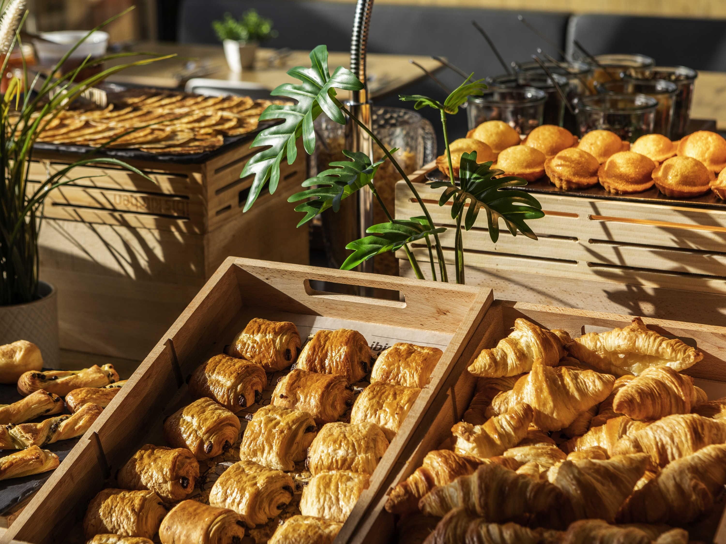 Forskellige bagværk, herunder croissanter og muffins, præsenteret i trækasser i et lyst rum med naturligt lys.