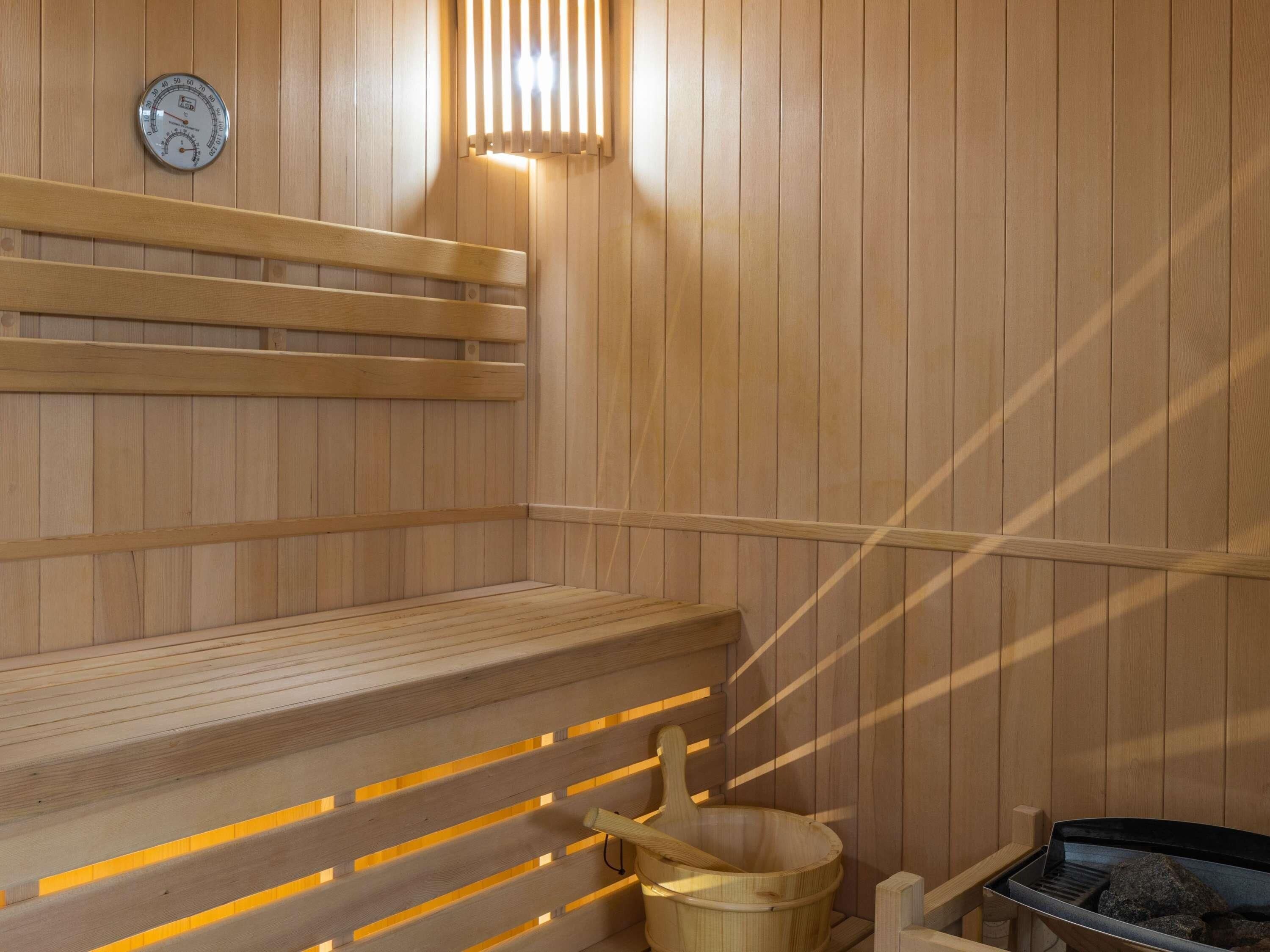 A sauna with wooden benches, a wooden bucket, and a heater.