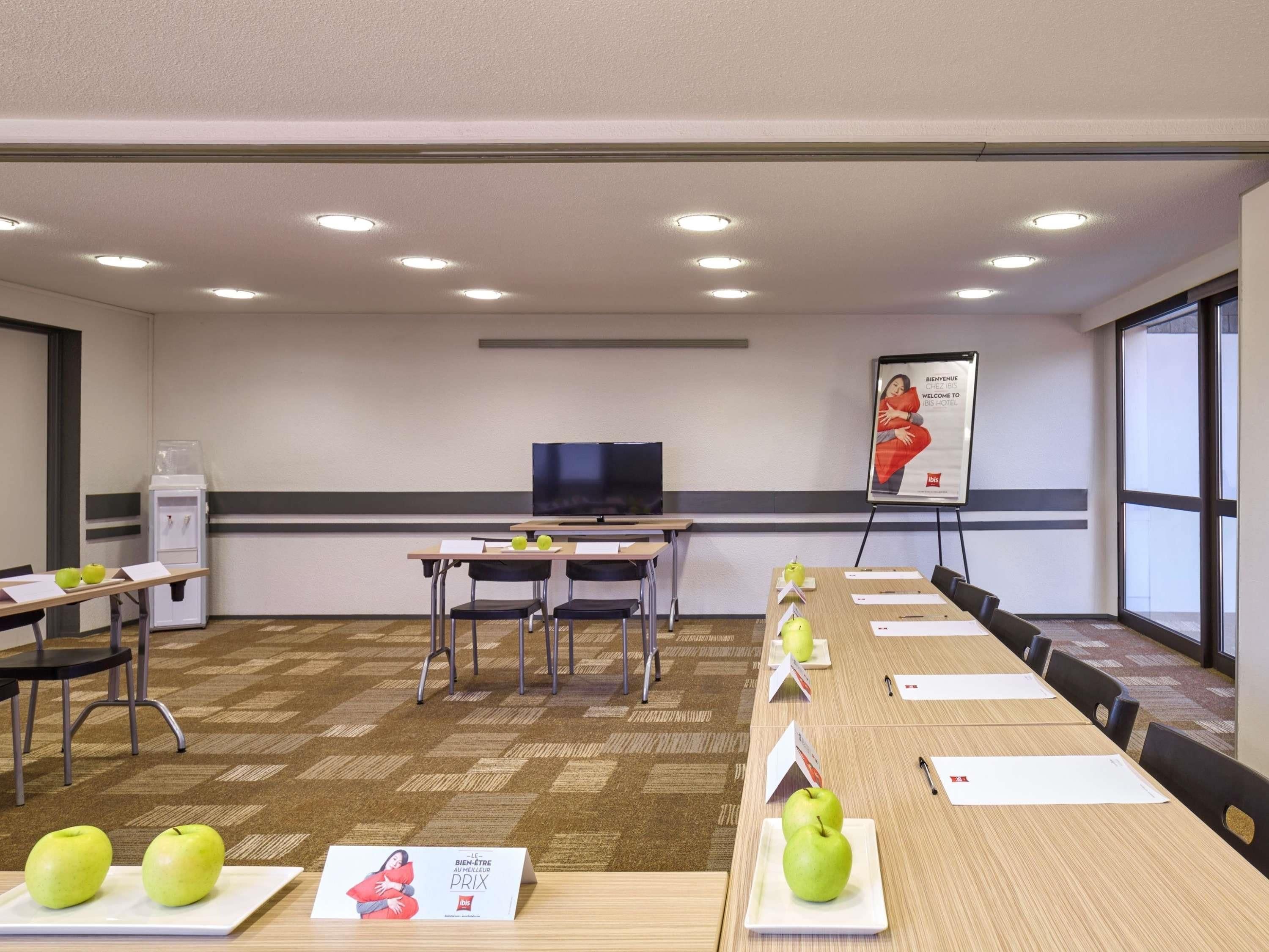 A conference room with a long table, chairs, a television, a whiteboard, and a poster on the wall.