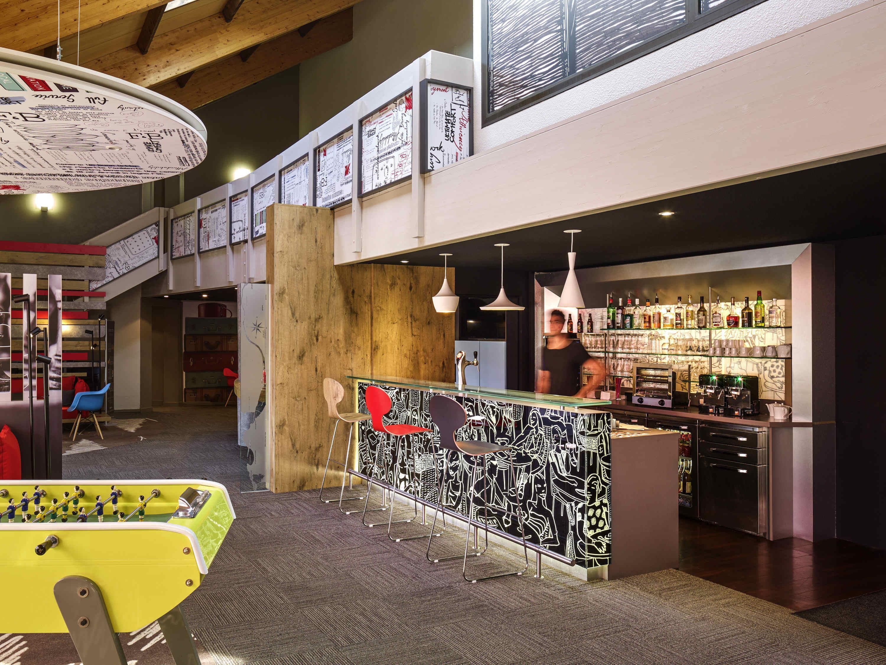 A bar area with a foosball table, a counter with a patterned design, and a shelf with bottles.