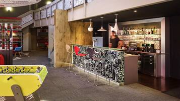A bar area with a foosball table, a counter with a patterned design, and a shelf with bottles.
