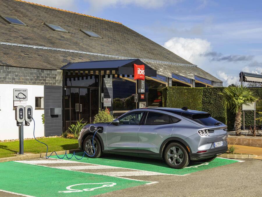 A car charging at a station in front of a building with a sign for 'ibis Hotels'.