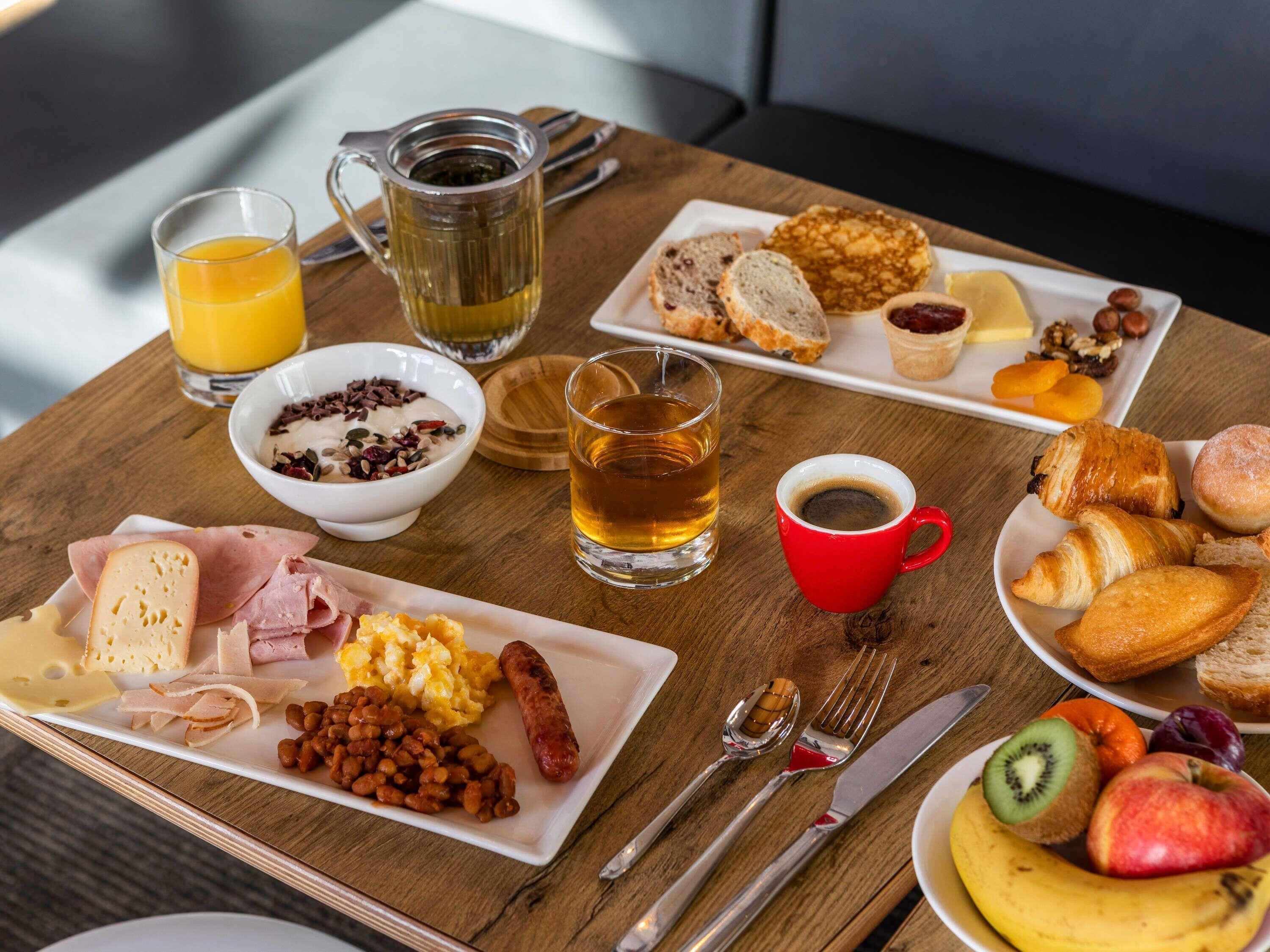 A breakfast table with plates of food, a mug of tea, a glass of orange juice, and cutlery.