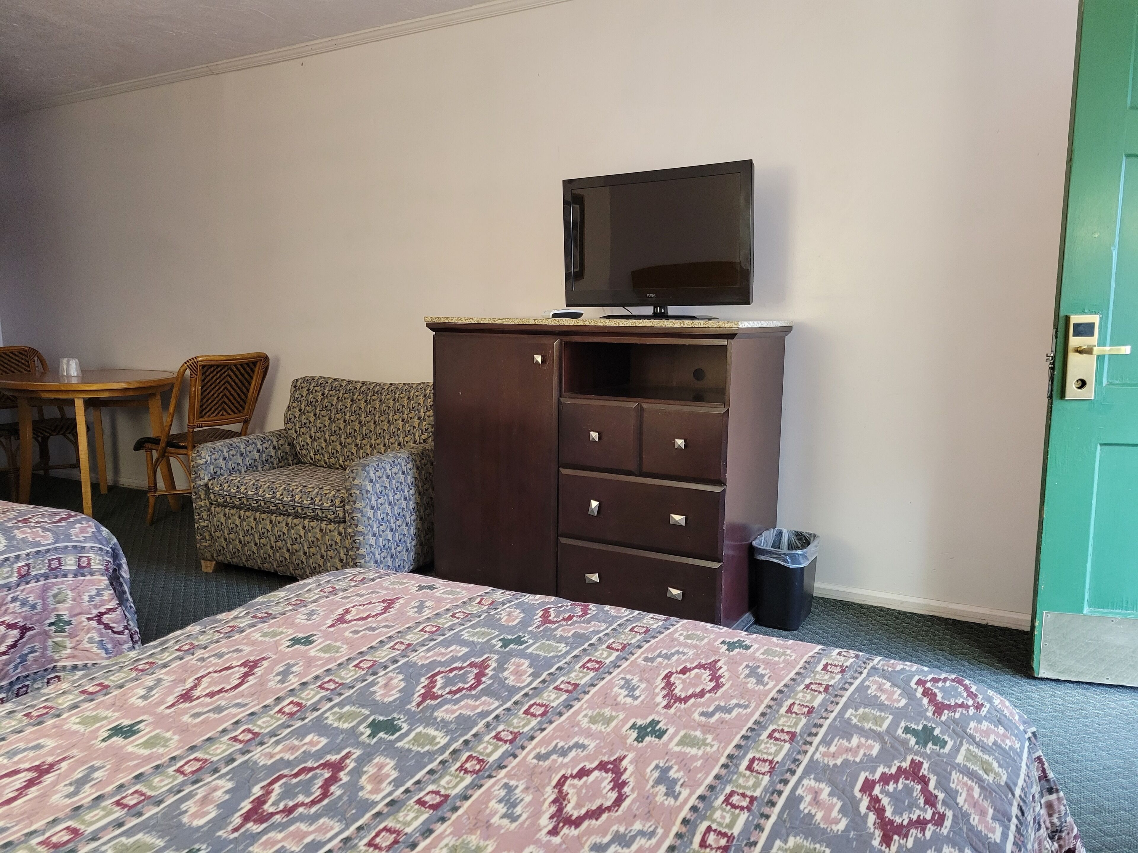 A hotel room with two beds, a wooden dresser, a television, a chair, and a small table.