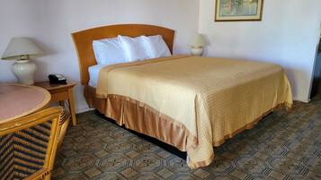 Una habitación de hotel con una cama, dos lámparas de noche, una silla de madera, una mesita pequeña y un suelo con diseño.