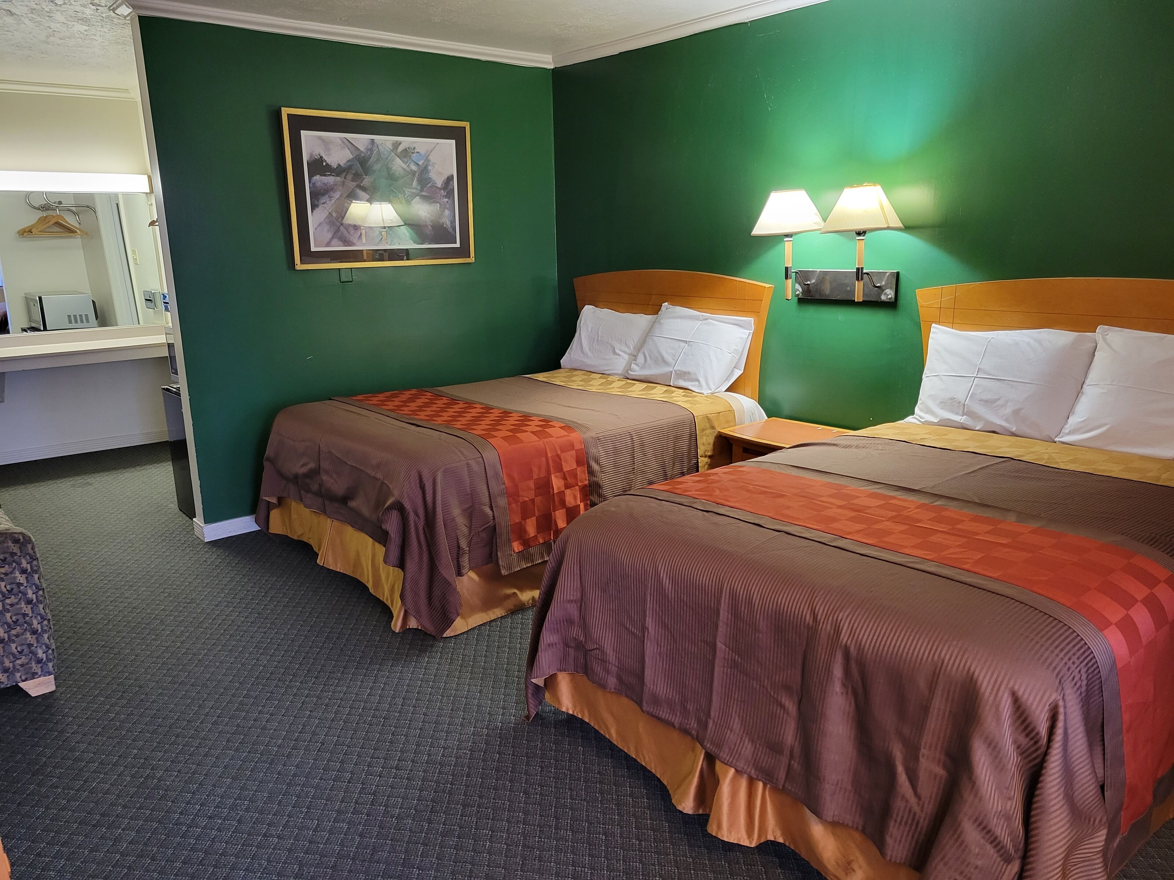 Habitación de hotel con dos camas, un escritorio, una silla, una lámpara y un cuadro en la pared.