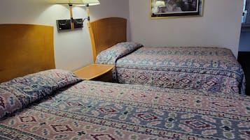 A hotel room with two beds, a wooden headboard, a small wooden table, and two wall-mounted lamps.