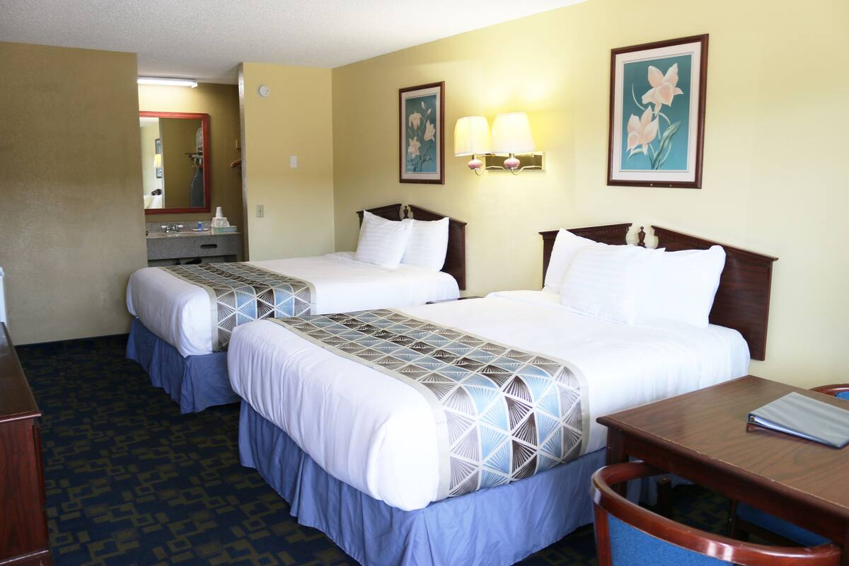 A hotel room with two beds, a desk, and a mirror.