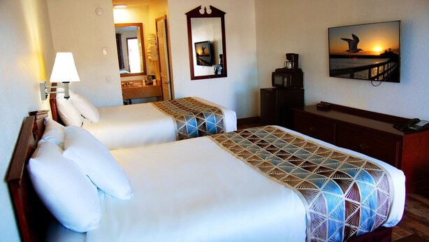 Quarto de hotel com duas camas, uma escrivaninha, um espelho, uma televisão e uma pintura de um pôr do sol.