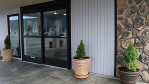 Entrada de um edifício com porta de vidro, vasos de plantas e parede de pedra.