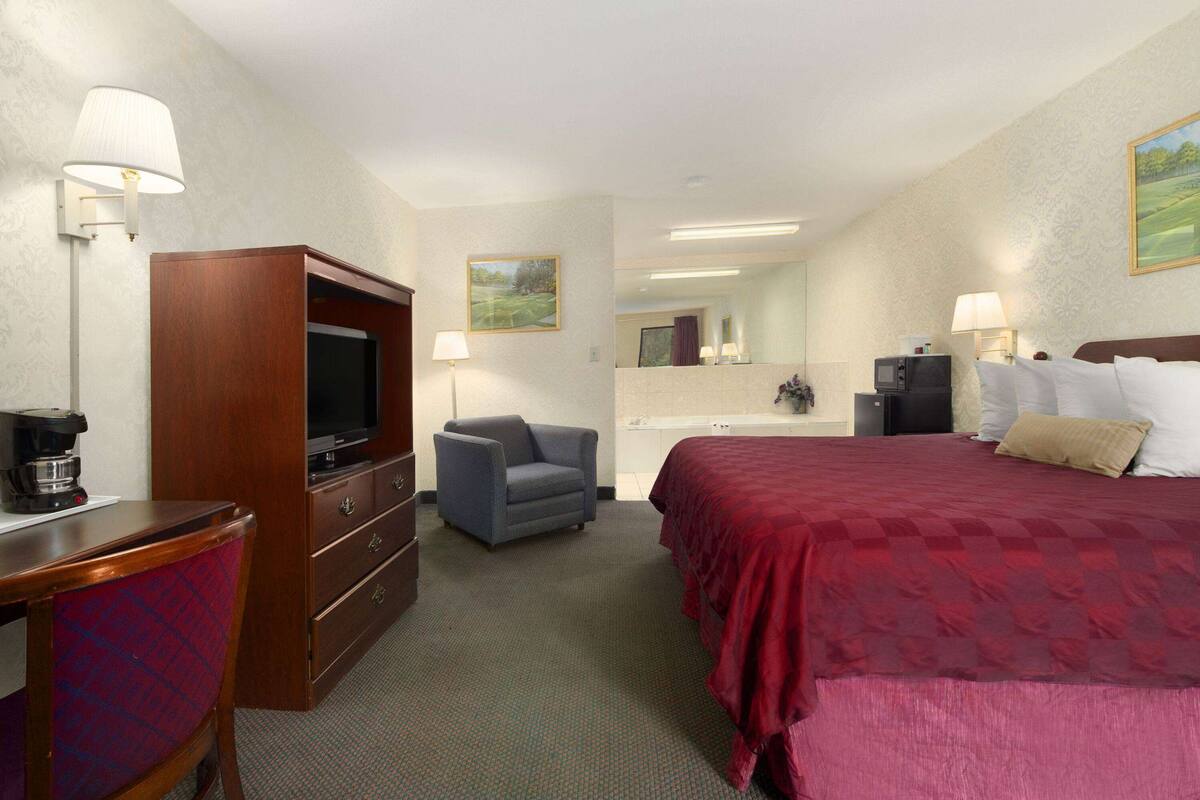 A hotel room with a bed, a desk with a television, a chair, a dresser, and a mirror.