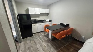 A compact kitchen with white cabinets, a black refrigerator, a microwave, and a coffee maker. There is a dining table with four orange chairs. - Days Inn by Wyndham Augusta / Fort Eisenhower (Augusta)