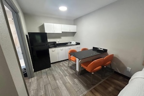 A compact kitchen with white cabinets, a black refrigerator, a microwave, and a coffee maker. There is a dining table with four orange chairs. - Days Inn by Wyndham Augusta / Fort Eisenhower (Augusta)