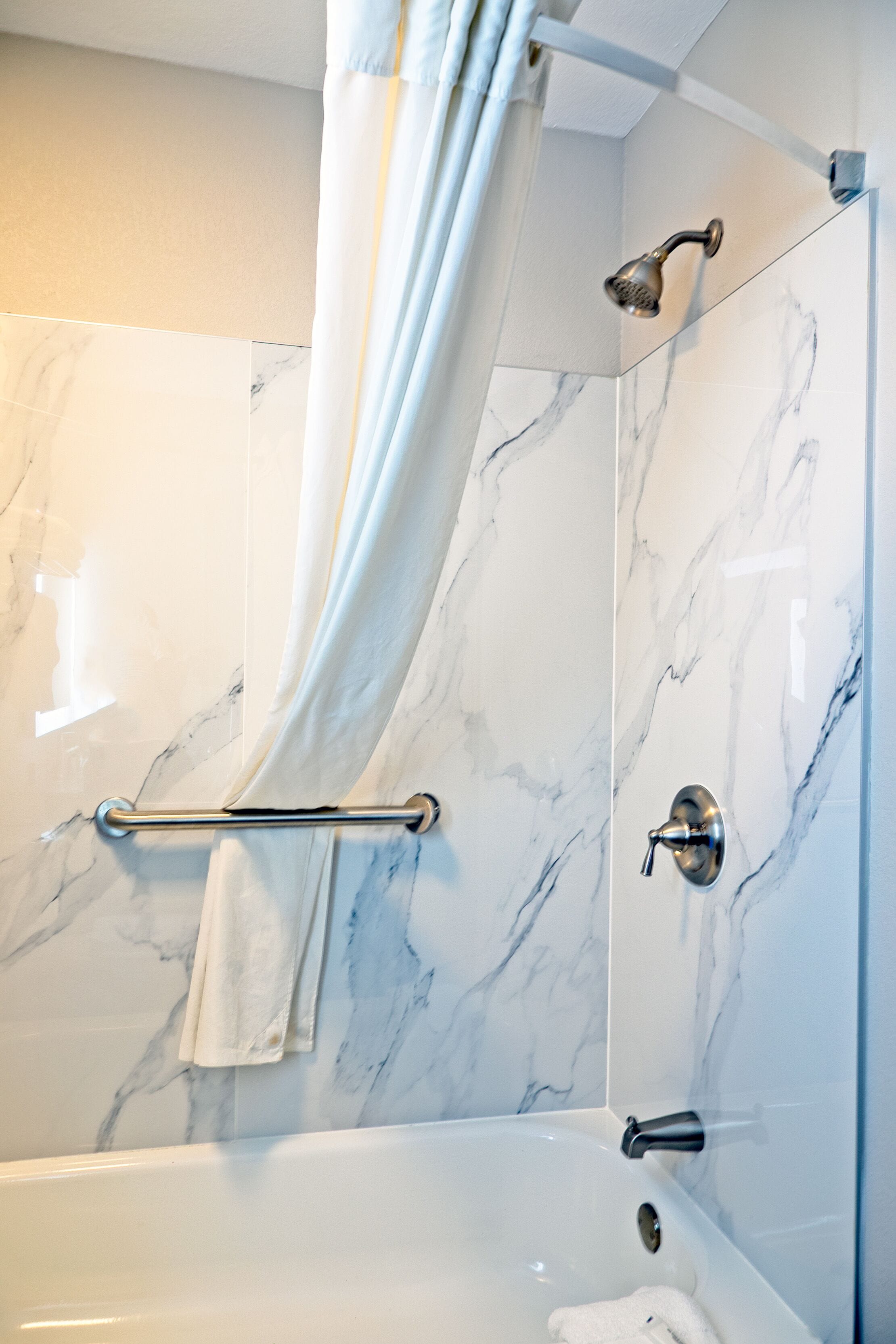 A modern bathroom with a marble wall, a bathtub, a showerhead, and a towel rack.