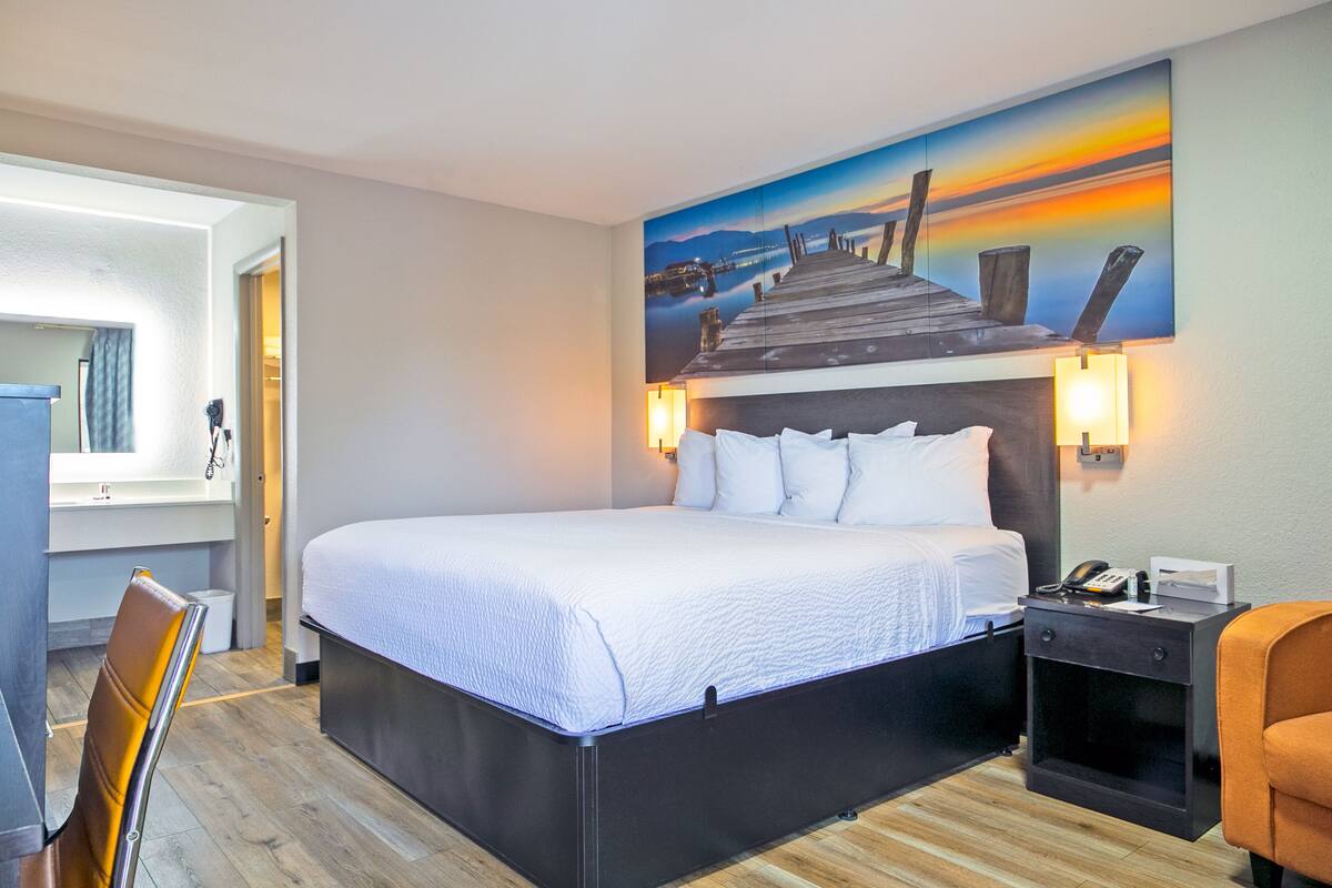 A hotel room with a large bed, a desk with a telephone, and a painting of a pier on the wall.