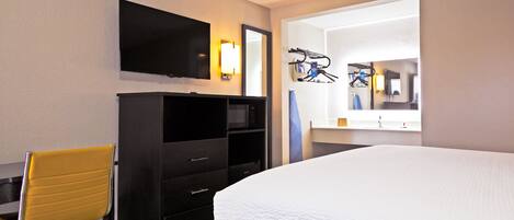 A hotel room with a bed, a TV mounted on the wall, a desk with a chair, and a mirror.