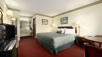 A hotel room with a bed, bedside table, lamp, and a television.