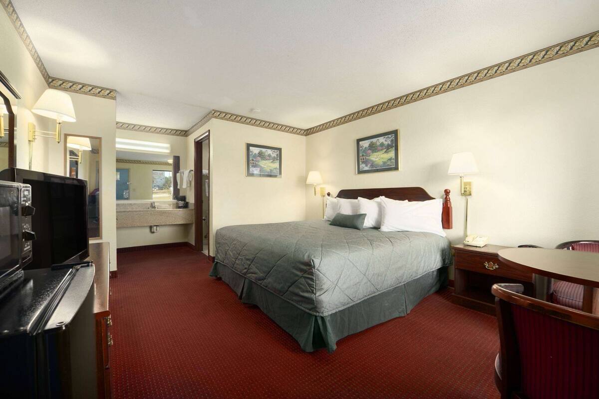 A hotel room with a bed, a desk, a chair, a television, a telephone, and a mirror.