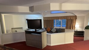 A hotel room with a bed, a desk with a TV, a sofa, and a window with curtains.