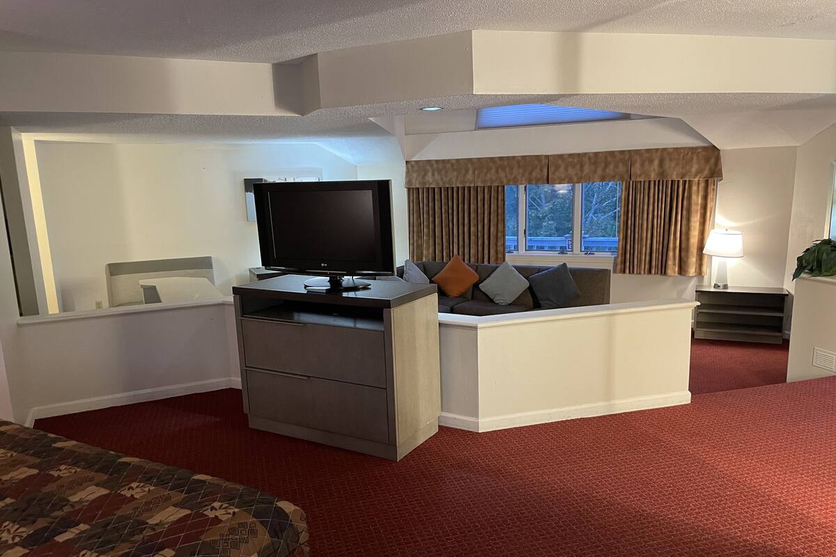 A hotel room with a bed, a desk with a TV, a sofa, and a window with curtains.