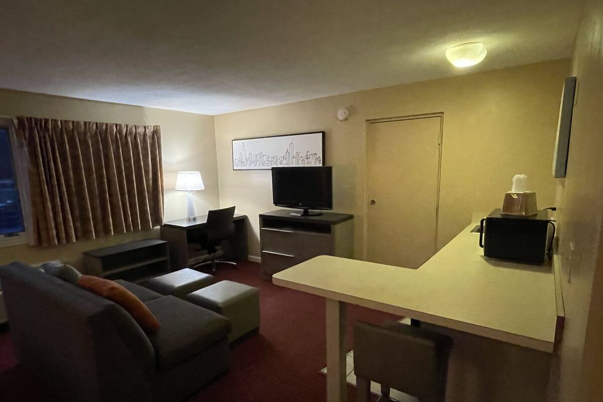 A hotel room with a sofa, a desk, a television, a lamp, and a painting on the wall.