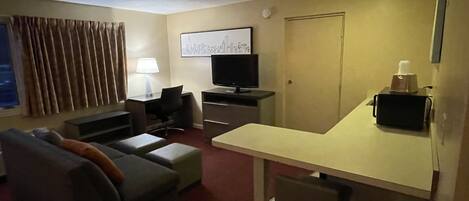 Habitación de hotel con sofá, escritorio, televisor, lámpara y un cuadro en la pared.
