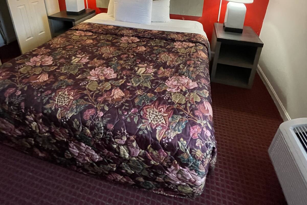 A hotel room with a large bed, two bedside tables with lamps, a red accent wall, and a modern abstract painting above the bed.