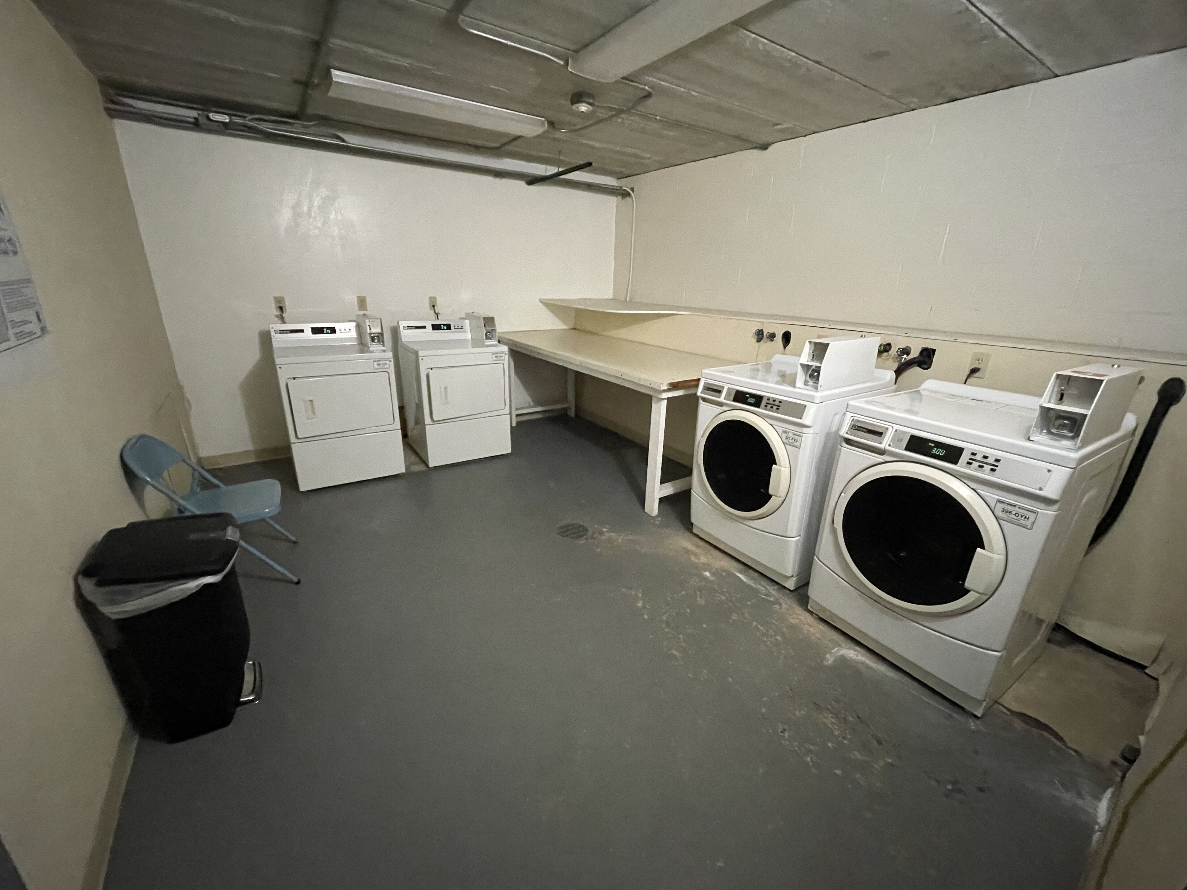 A laundry room with two washing machines, a drying machine, a sink, and a chair.
