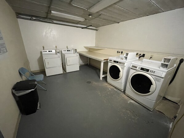 A laundry room with two washing machines, a drying machine, a sink, and a chair.