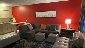 A modern living room with a sectional sofa, ottomans, a coffee table, a red accent wall, and a cityscape artwork.