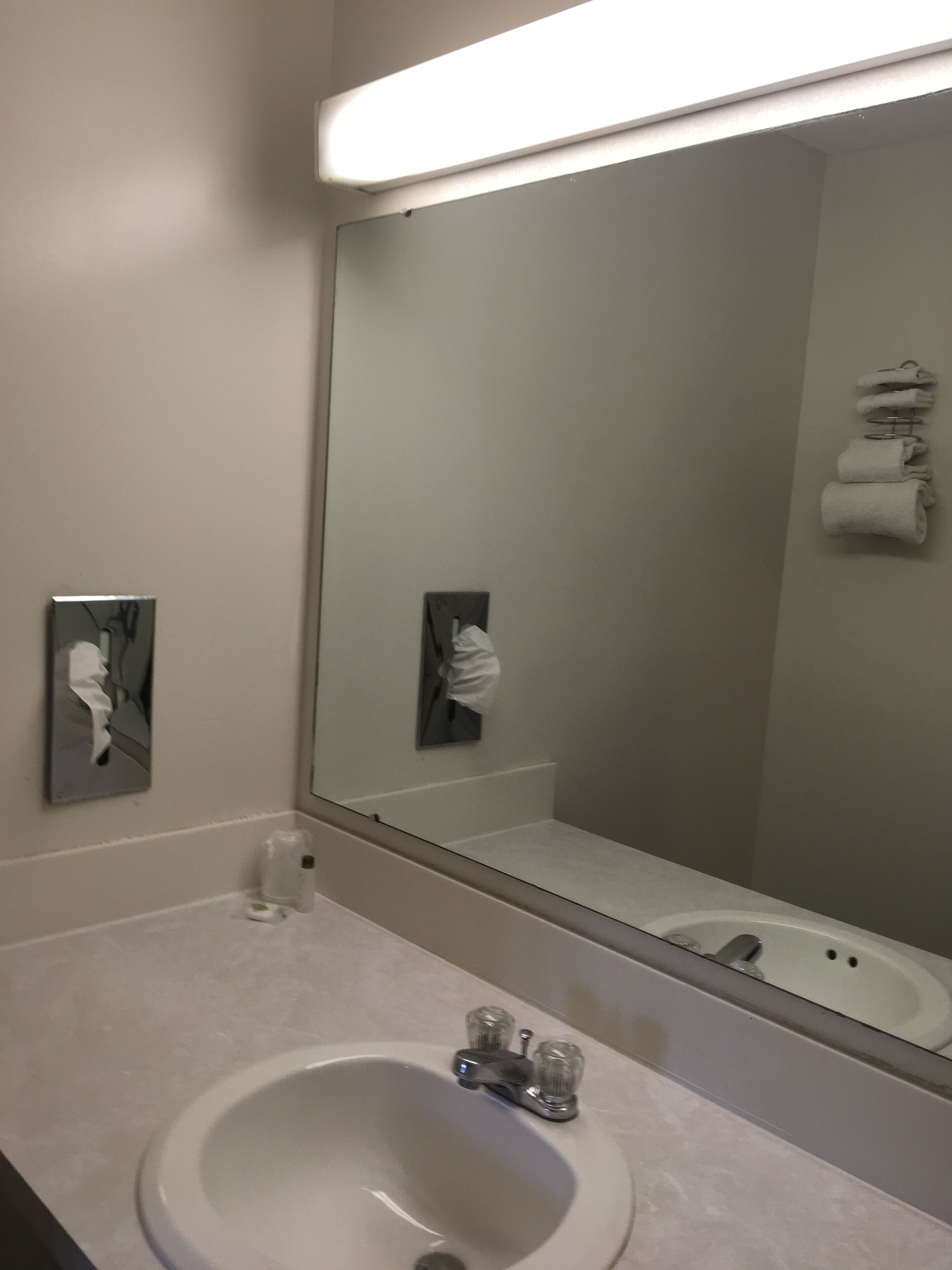 Un baño con un espejo grande, un lavamanos y un perchero para toallas.