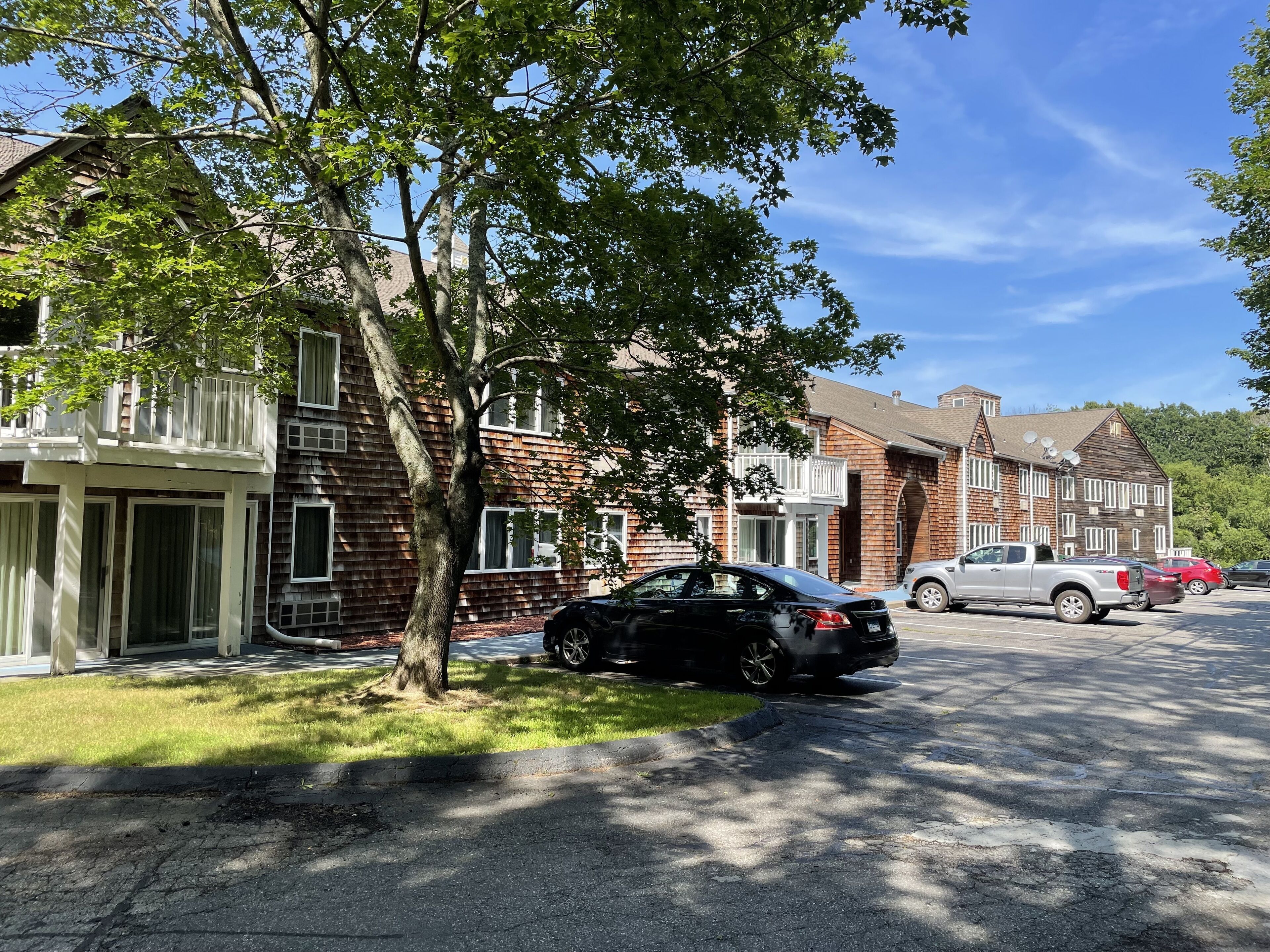 A residential street with brick houses, a black car parked on the side, and a silver pickup truck.